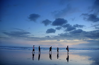 Silhouettes of people standing on wet beach at twilight