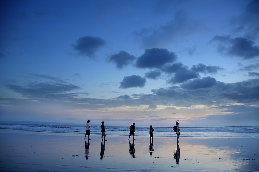Silhouettes of people standing on wet beach at twilight