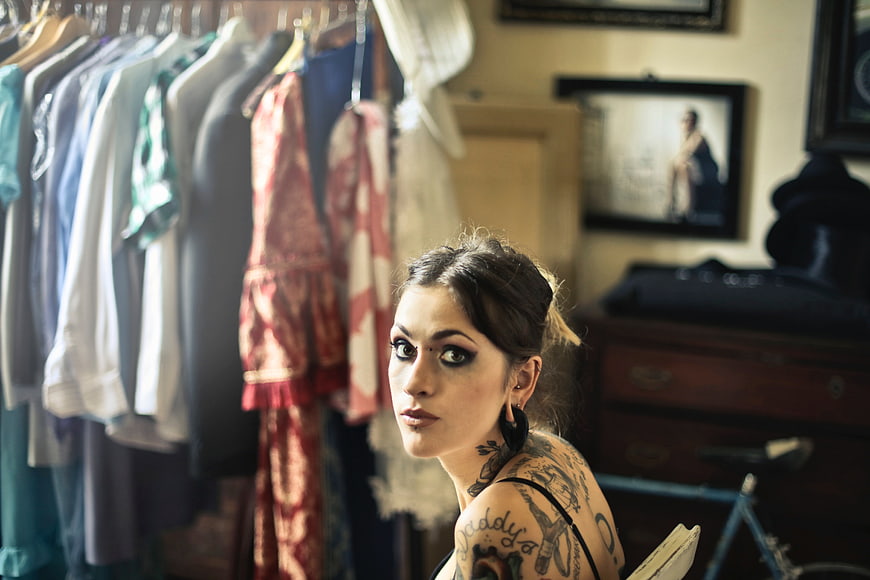 Tattooed woman with dark makeup looking back in vintage room