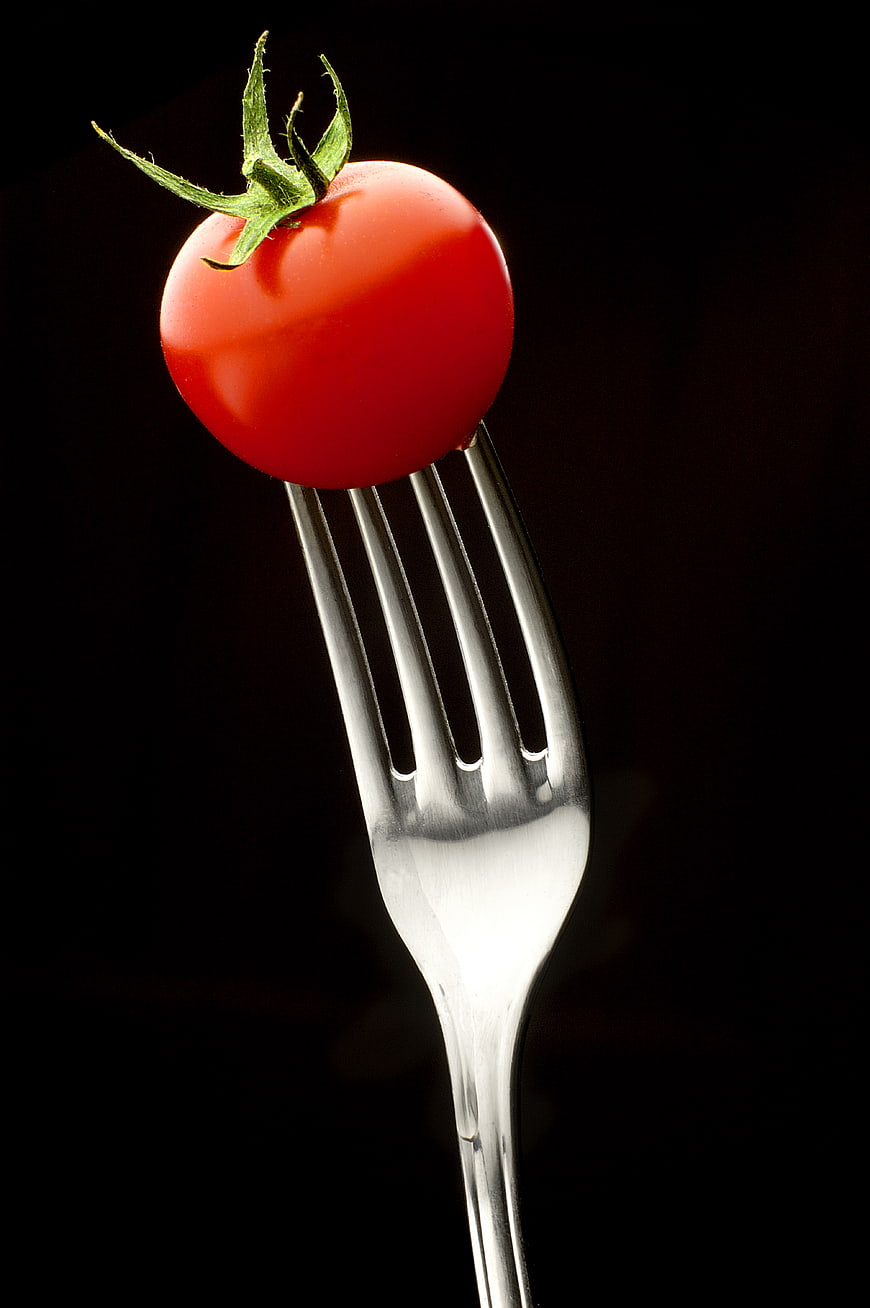 Fresh Red Cherry Tomato on Silver Fork Against Black Background