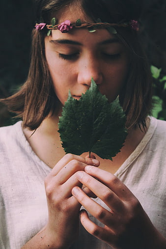 Girl with flower crown smelling green leaf in nature