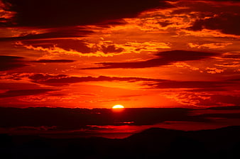 Fiery red sunset with dramatic clouds over dark mountain silhouette