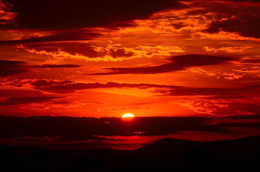 Fiery red sunset with dramatic clouds over dark mountain silhouette