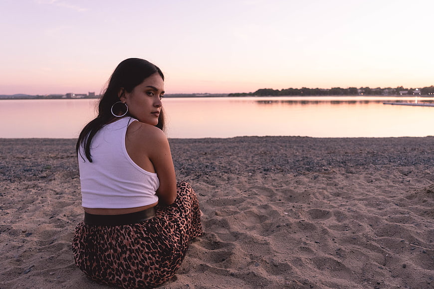 Woman Sitting on Sandy Beach at Sunset Looking Back