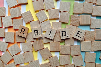 Pride spelled with wooden Scrabble tiles on rainbow background
