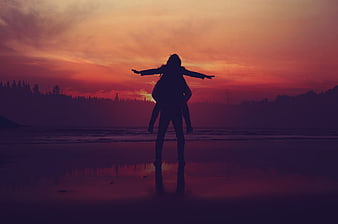 Silhouette of couple on beach at sunset with arms outstretched