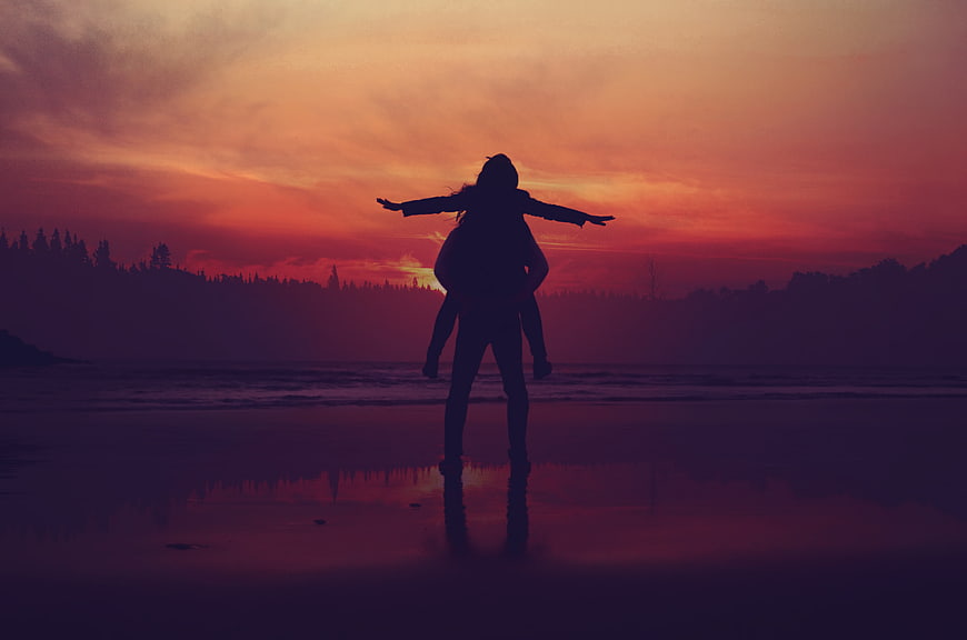Silhouette of couple on beach at sunset with arms outstretched