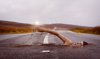 Surreal swimmer performing freestyle stroke on wet asphalt road