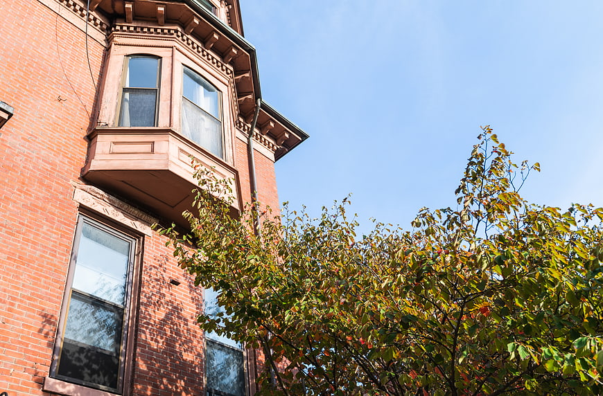 Low angle view of red brick building with bay window and autumn tree