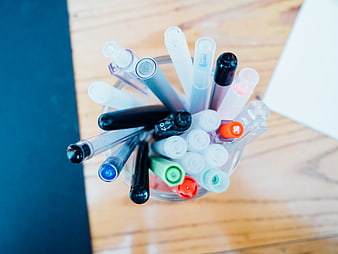 Top View of Colorful Pens in Glass Cup on Wooden Desk