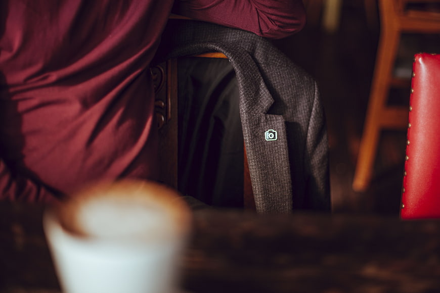 Close-up of grey blazer with camera pin in cafe
