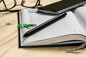 Open planner with pen, smartphone, and glasses on wooden desk