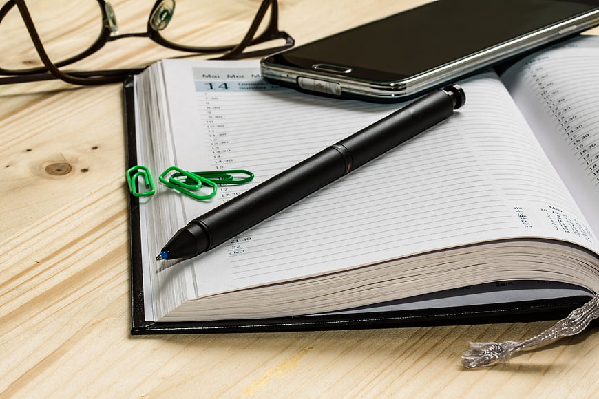 Open planner with pen, smartphone, and glasses on wooden desk