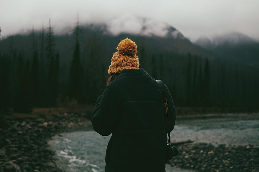 Woman in yellow beanie looking at misty mountains