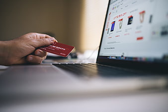 Hand holding red credit card near laptop for online shopping