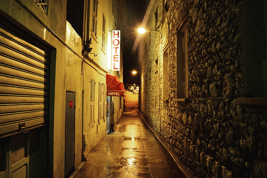 Narrow European alleyway at night with glowing hotel sign