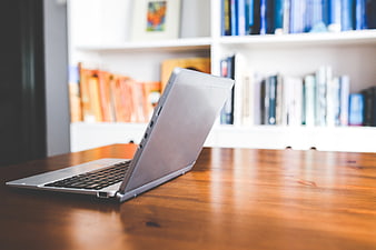 Silver laptop on wooden desk with blurred bookshelf background