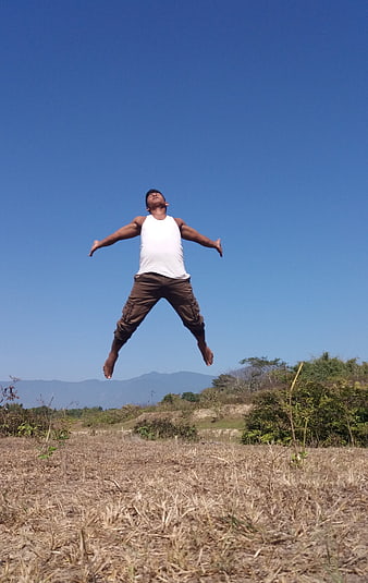 Young man jumping in dry field with blue sky