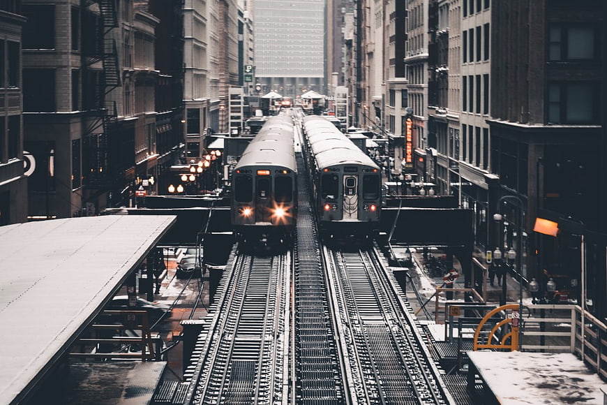 Two subway trains on elevated tracks in a snowy city