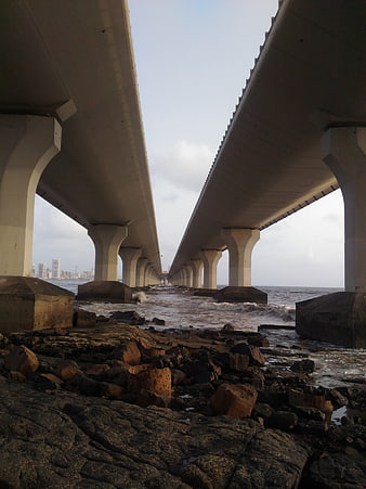 Low angle view under concrete bridge pillars by rocky shore