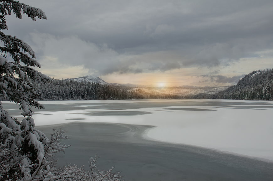 Serene Frozen Lake Landscape with Snowy Forest and Sunset