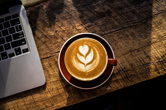 Overhead view of latte art coffee and laptop on rustic wooden table