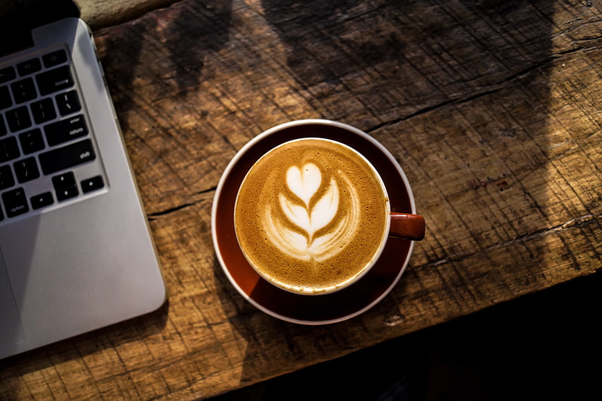 Overhead view of latte art coffee and laptop on rustic wooden table