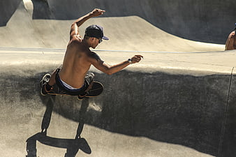 Shirtless Skateboarder Performing Trick in Concrete Skatepark