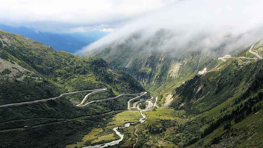Winding mountain road through green valley with clouds