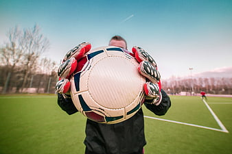 Goalkeeper holding soccer ball on green field
