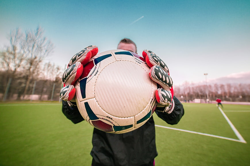 Goalkeeper holding soccer ball on green field