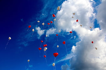 Red and white heart balloons floating in blue sky