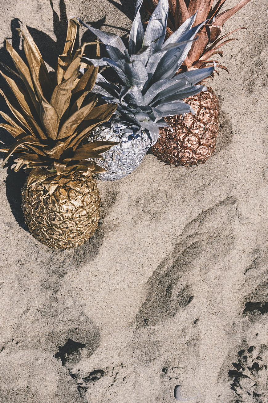 Metallic gold, silver, and copper pineapples on sand