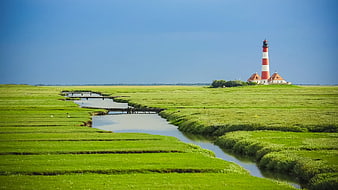 Red and white lighthouse in green marshland with winding river