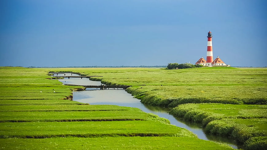 Red and white lighthouse in green marshland with winding river