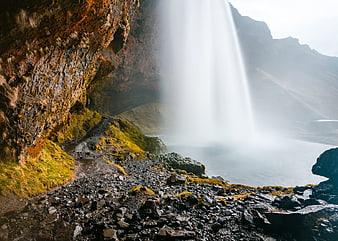Hiker walking behind a powerful waterfall in Iceland