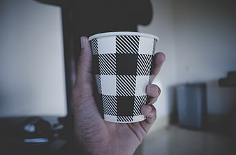 Hand holding black and white checkered paper coffee cup