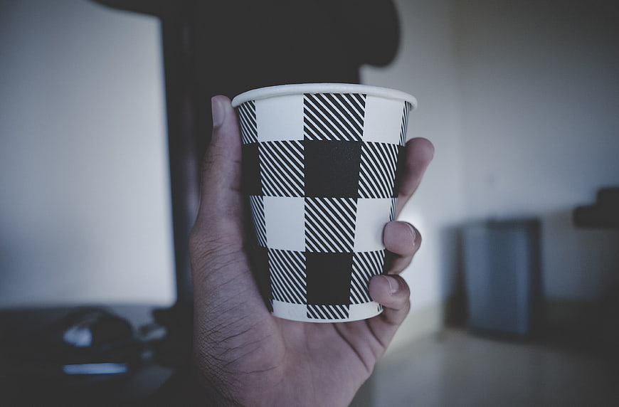 Hand holding black and white checkered paper coffee cup