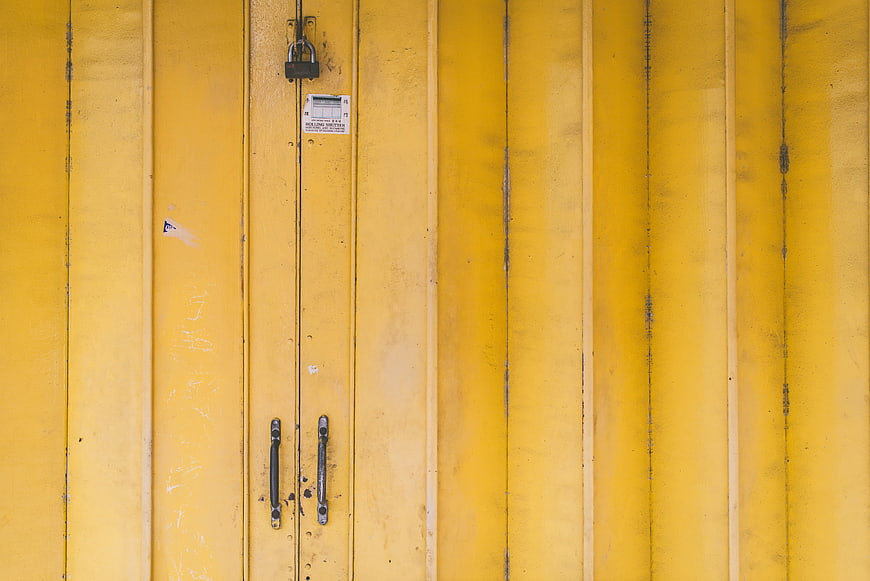 Close-up of weathered yellow metal doors with padlock