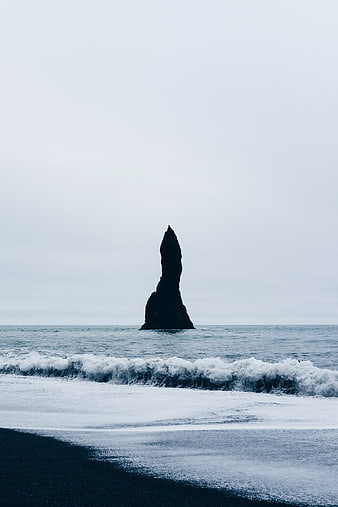 Solitary sea stack on black sand beach with crashing waves