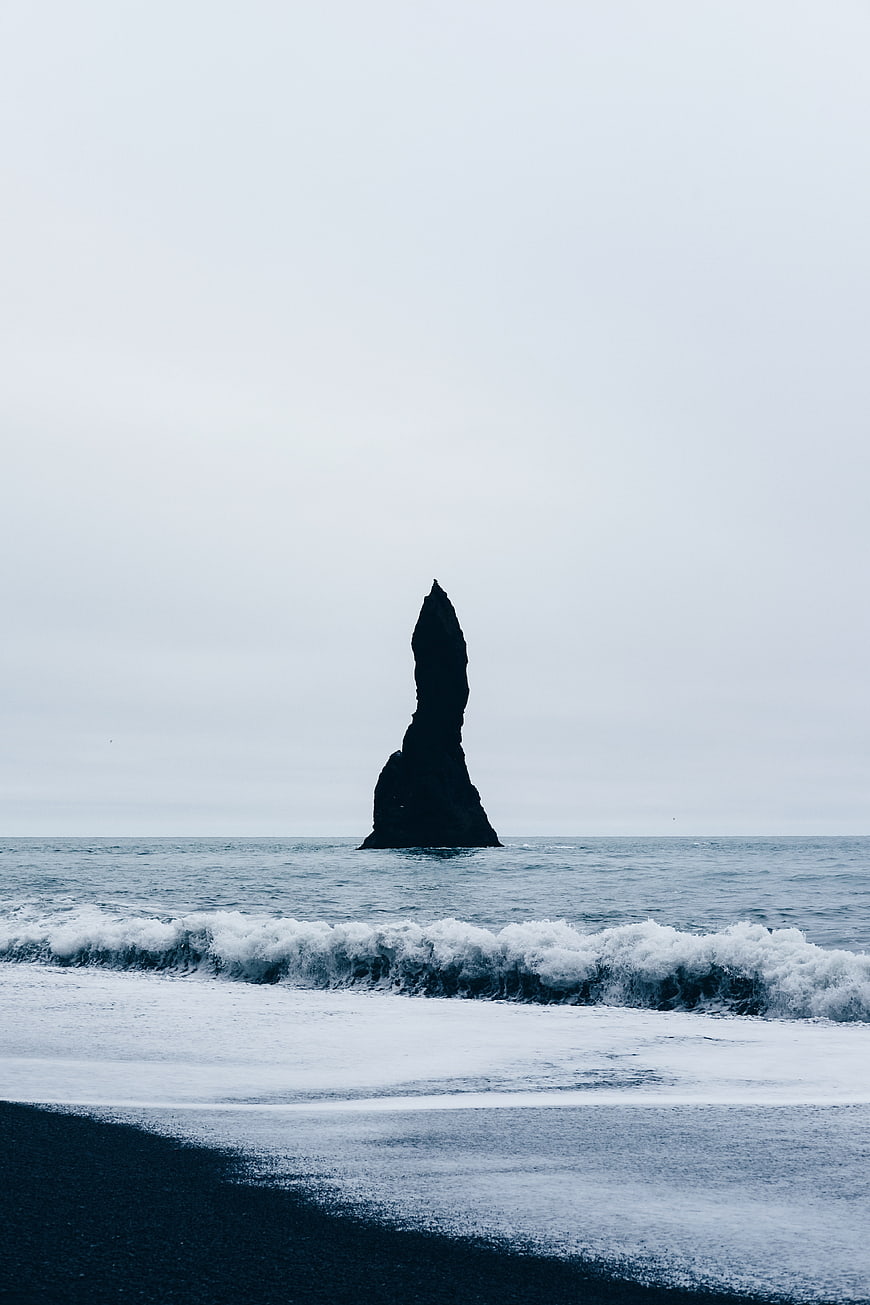 Solitary sea stack on black sand beach with crashing waves