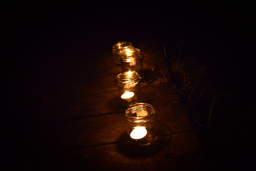 Tea lights in glass jars on wooden planks at night