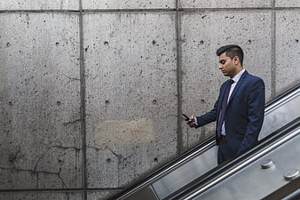 Businessman in Blue Suit Checking Smartphone on Escalator
