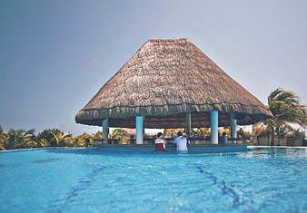 Tropical resort infinity pool with thatched bar and relaxing couple