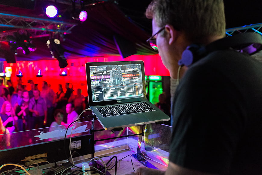 DJ operating laptop with audio software at a vibrant nightclub concert