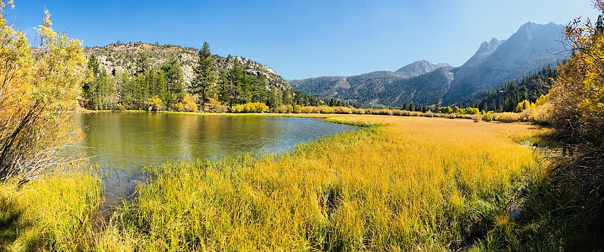 Panoramic autumn landscape with golden grass, lake, and mountains