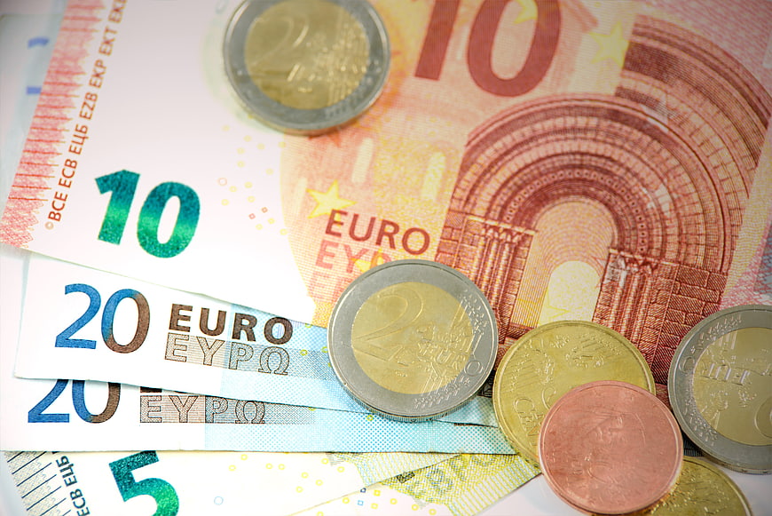 Euro banknotes and coins scattered on white background