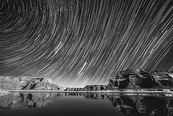 Black and white star trails over desert canyon with water reflection