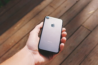 Hand holding silver iPhone on wooden deck background