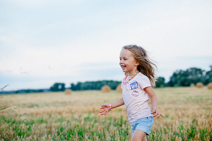Happy little girl running through a golden summer field